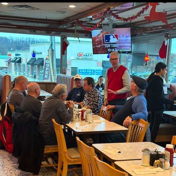 Diner interior with patrons seated at tables, Christmas decorations, and a TV screen showing baseball.