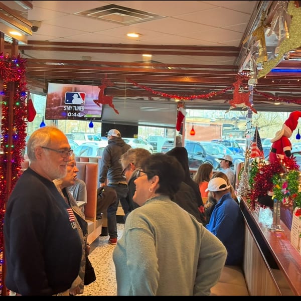 Diner interior with patrons, Christmas decorations, and a TV screen showing a baseball logo.